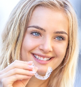 A young girl holding a clear aligner and smiling