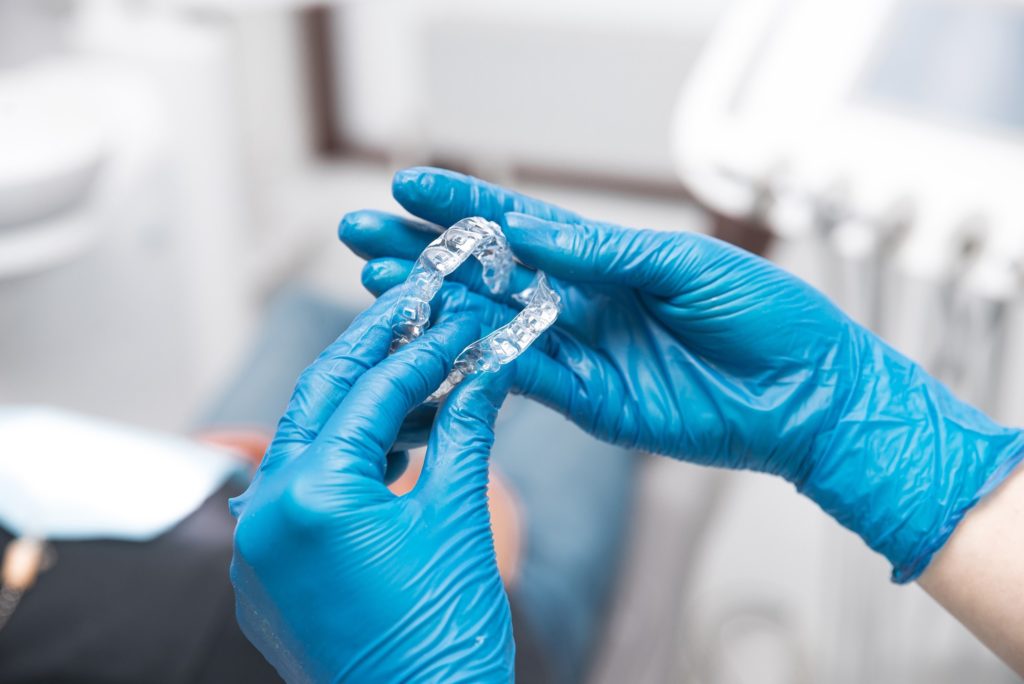 Dentist holding clear aligners with blue gloves